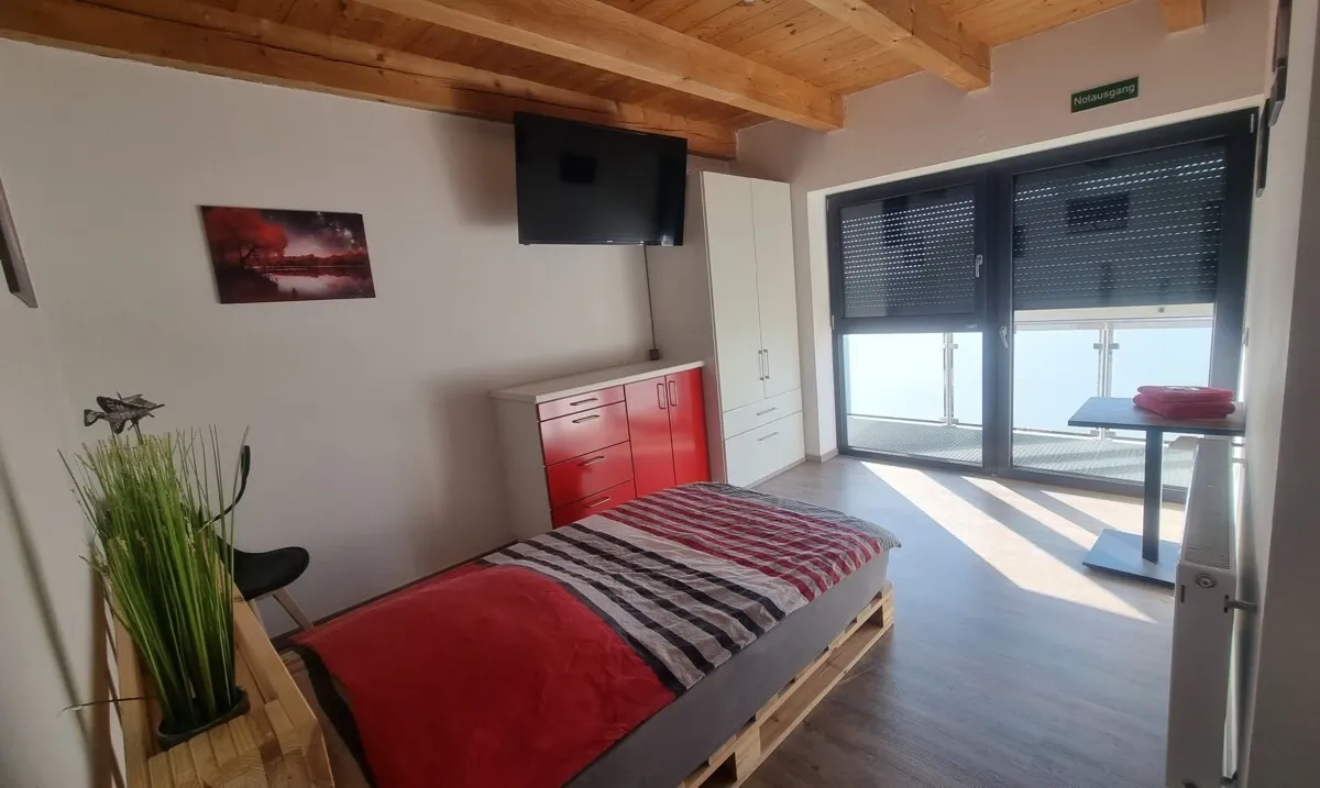 Zimmer mit rot bezogenem Bett und Zugang zum Balkon